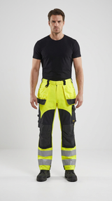Mand i sort t-shirt og neongule arbejdsbukser med reflekser mod en hvid baggrund.
