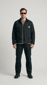 Mand i sort Carhartt-jakke, arbejdsbukser og solbriller mod en lys grå baggrund.