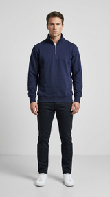 Mand i mørkeblå sweatshirt med lynlås, mørke bukser og hvide sneakers mod en grå baggrund.