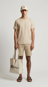 Mand i beige t-shirt, shorts og kasket holder en mulepose med logoet for Den Digitale Bondegård.