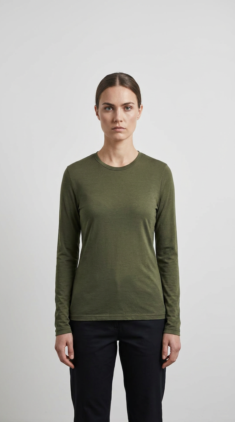 Kvinde iført en olivengrøn langærmet t-shirt og mørke bukser mod en enkel, lys baggrund.