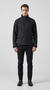 Mand iført sort softshell-jakke med røde detaljer og sorte bukser på en lys baggrund.