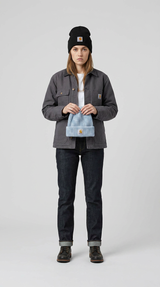 Kvinde i grå Carhartt-jakke og sort hue, der holder en lyseblå hue mod en grå baggrund.
