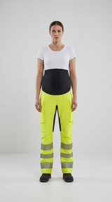 Gravid kvinde i hvid t-shirt og neon-gule high-vis arbejdsbukser med sort mavepanel.