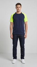 Mand i mørkeblå t-shirt med neongule ærmer, mørke jeans og hvide sneakers foran en grå baggrund.