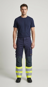 Mand i mørkeblå t-shirt og arbejdsbukser med neongule detaljer og reflekser foran en hvid baggrund.