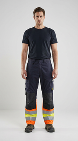 Mand i sort t-shirt og mørkeblå arbejdsbukser med orange og gule refleksbånd mod en lys grå baggrund.