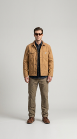 Mand i lysebrun Carhartt-jakke, denimskjorte, brune arbejdsbukser og solbriller mod en grå baggrund.