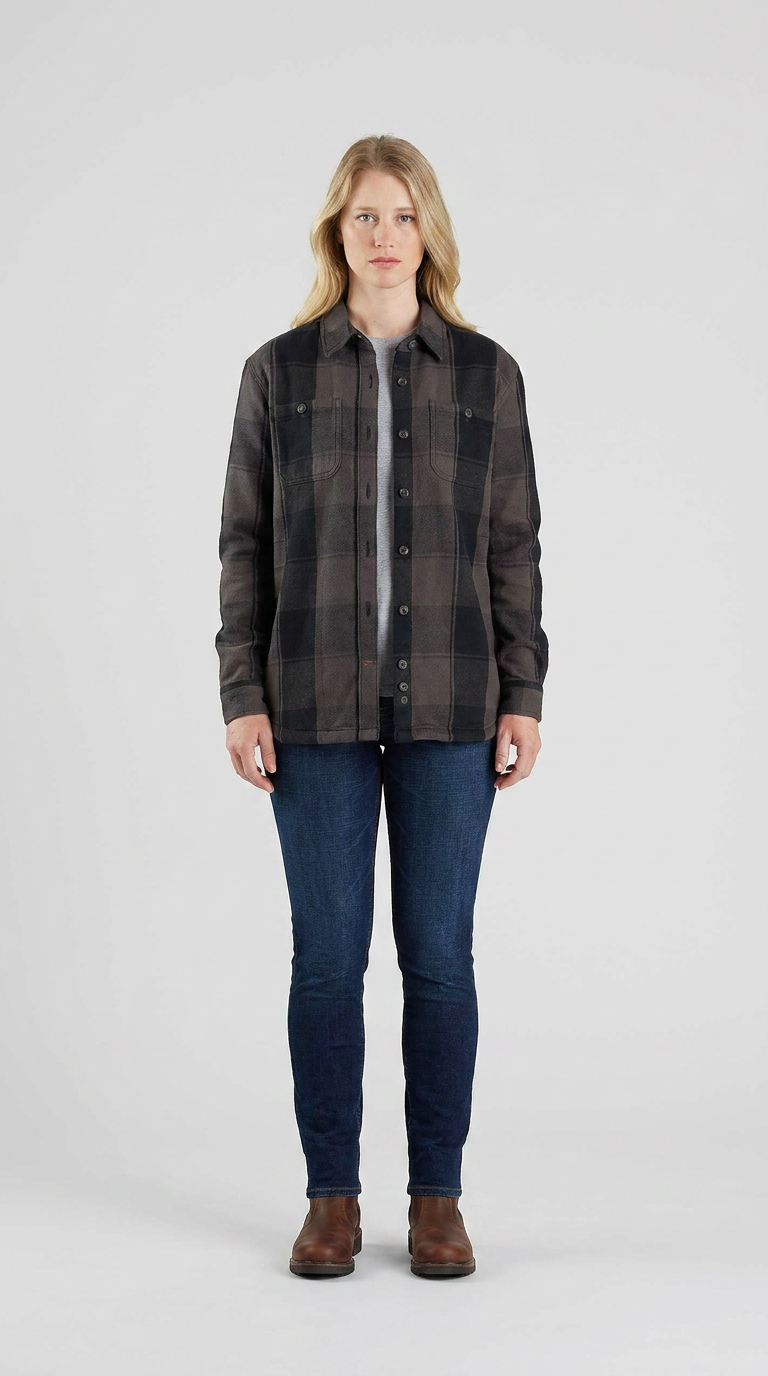 Kvinde i mørk ternet skjorte, blå jeans og brune støvler mod en lys baggrund.