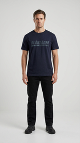 Mand iført mørkeblå t-shirt med Blåkläder-logo og sorte bukser mod en lys baggrund.