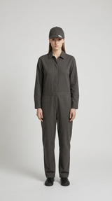 Kvinde i mørkegrå langærmet jumpsuit og matchende kasket mod en lys grå baggrund.
