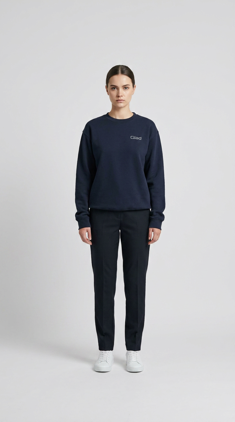Kvinde i mørkeblå sweatshirt med Glad-logo, mørke bukser og hvide sneakers på en hvid baggrund.
