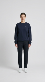 Kvinde i mørkeblå sweatshirt med Glad-logo, mørke bukser og hvide sneakers på en hvid baggrund.