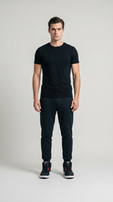Mand i sort t-shirt, sorte joggingbukser og sneakers stående foran en lys grå baggrund.