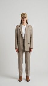 Kvinde iført beige jakkesæt, hvid t-shirt og kasket stående mod en neutral baggrund.