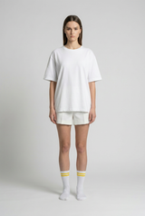 Kvinde i en oversized hvid t-shirt og shorts med stribede sokker på en neutral grå baggrund.