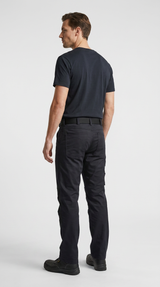 Mand set bagfra iført sort t-shirt og sorte arbejdsbukser mod en hvid baggrund.