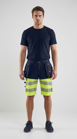 Mand i sort t-shirt og mørkeblå arbejdsshorts med neon-gul high-vis og reflekser på hvid baggrund.