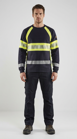 Mand i mørkeblå sweatshirt med gule reflekser og arbejdsbukser foran en lys baggrund.