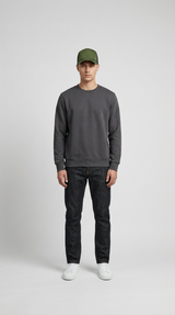 Mand i mørkegrå sweatshirt, mørke jeans, hvide sneakers og en grøn kasket mod en lys baggrund.
