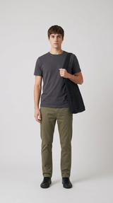 Mand iført mørkegrå t-shirt, olivengrønne chinos og sort mulepose mod en lys baggrund.